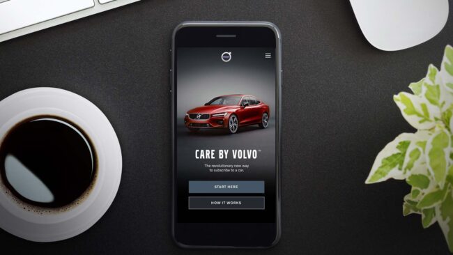 téléphone sur une table à côté d'une plante et d'une tasse à café affichant l'écran d'accueil de la plateforme de vente au détail numérique care by volvo